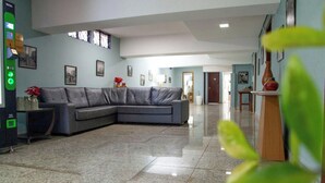 A spacious living room with a grey sectional sofa, a coffee machine, and framed pictures on the walls. - Londres Royal Hotel (Londrina)