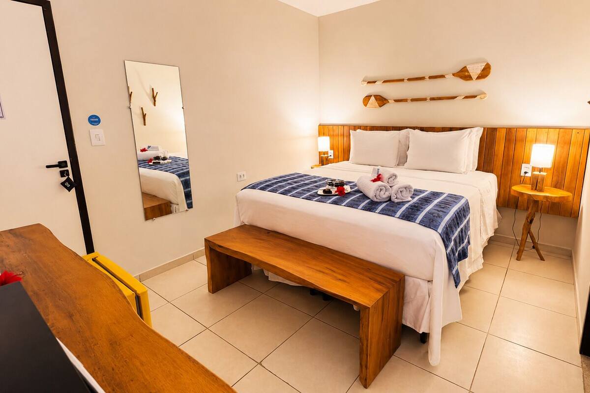 Ein Hotelzimmer mit einem Bett, einer Bank, einem Schreibtisch, einem Spiegel und einem Wandregal.