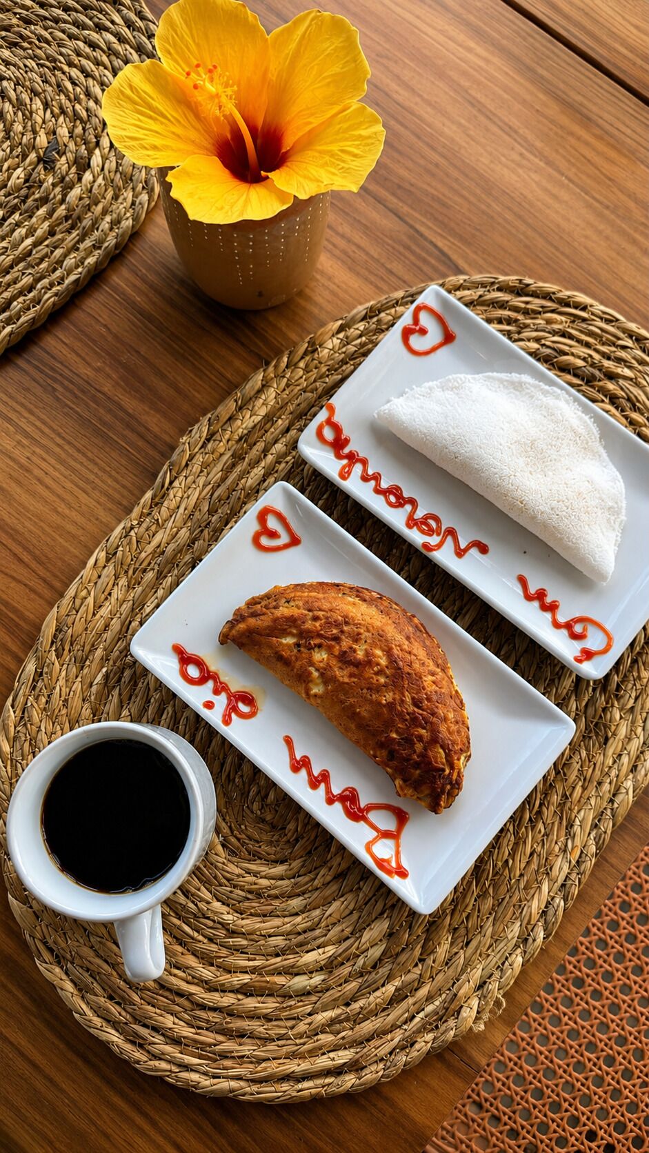 Una tovaglietta intrecciata con un piatto bianco che contiene un cibo fritto, un tovagliolo bianco e una tazza di caffè nero.