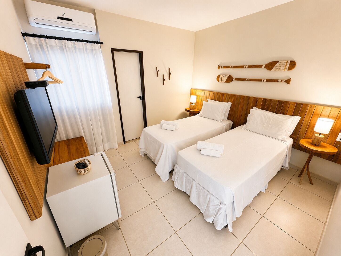 A hotel room with two beds, a TV, a desk, a small table, and a wall-mounted guitar.