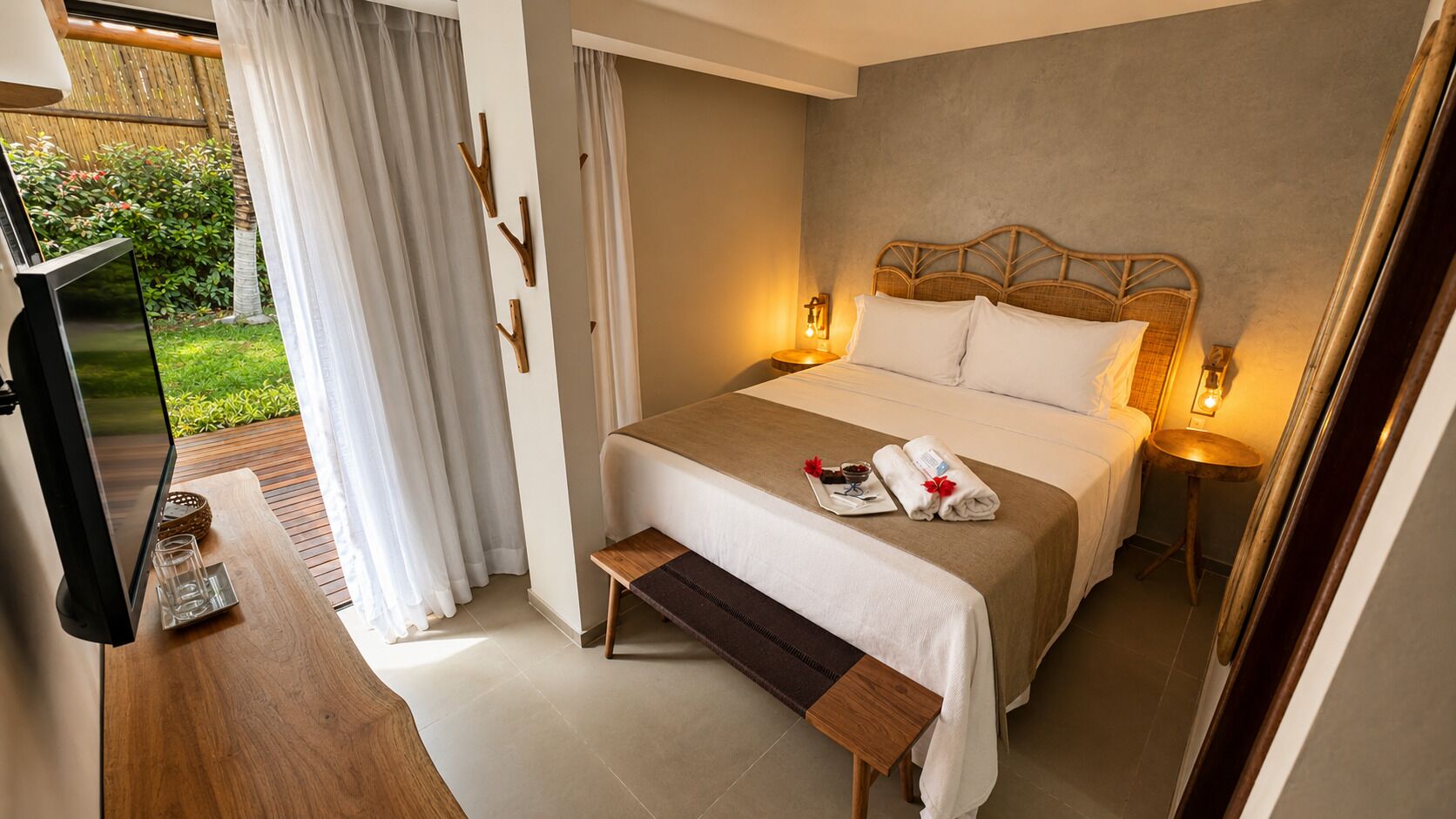 Una habitación de hotel con cama, mesita de noche, lámpara y televisor.