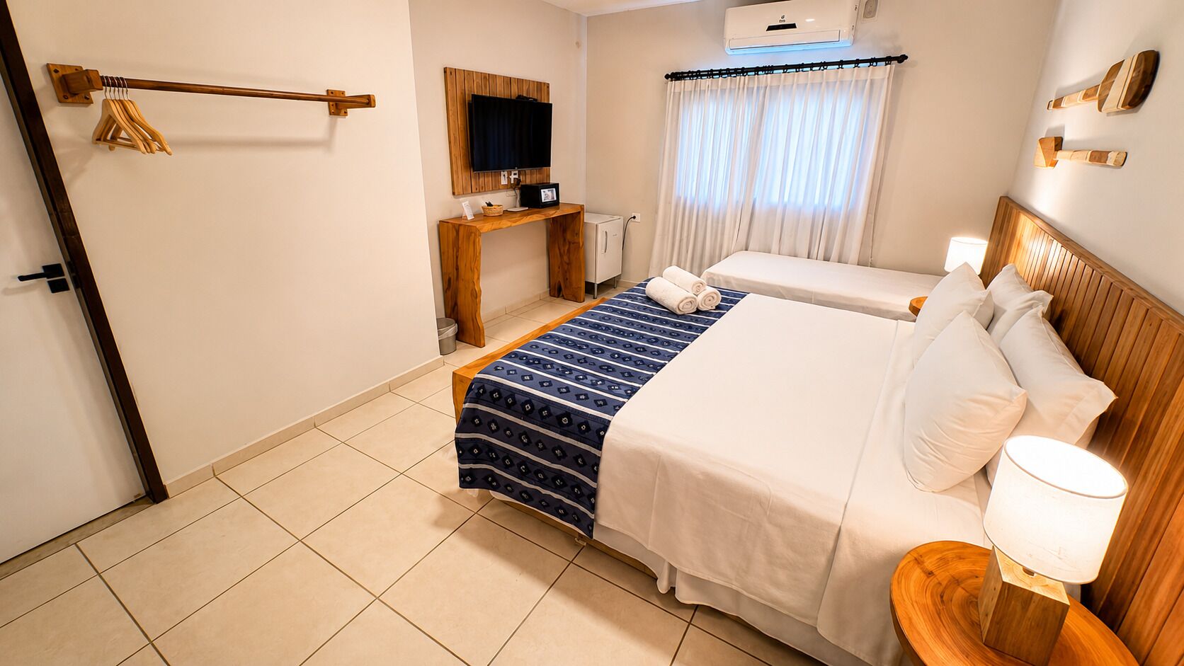 Une chambre d’hôtel comprenant un lit, une table de chevet, une lampe, une télévision et un bureau avec une chaise.