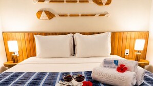 A hotel room with a wooden headboard, a bed with white linens, a blue striped bedspread, a tray with chocolates and a red flower, and a towel with a logo. - Pousada Estrela Lunar Noronha by Alto da Ilha (Fernando de Noronha)