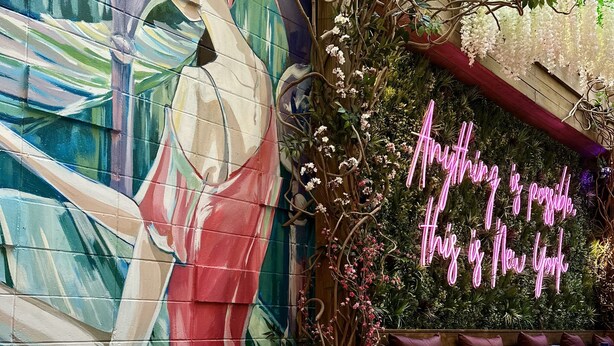Un área de comedor al aire libre con mesas redondas, sillas y un mural en la pared.