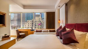 Habitación de hotel con una cama grande, un escritorio y una silla. Se ve una ventana con vistas a edificios.