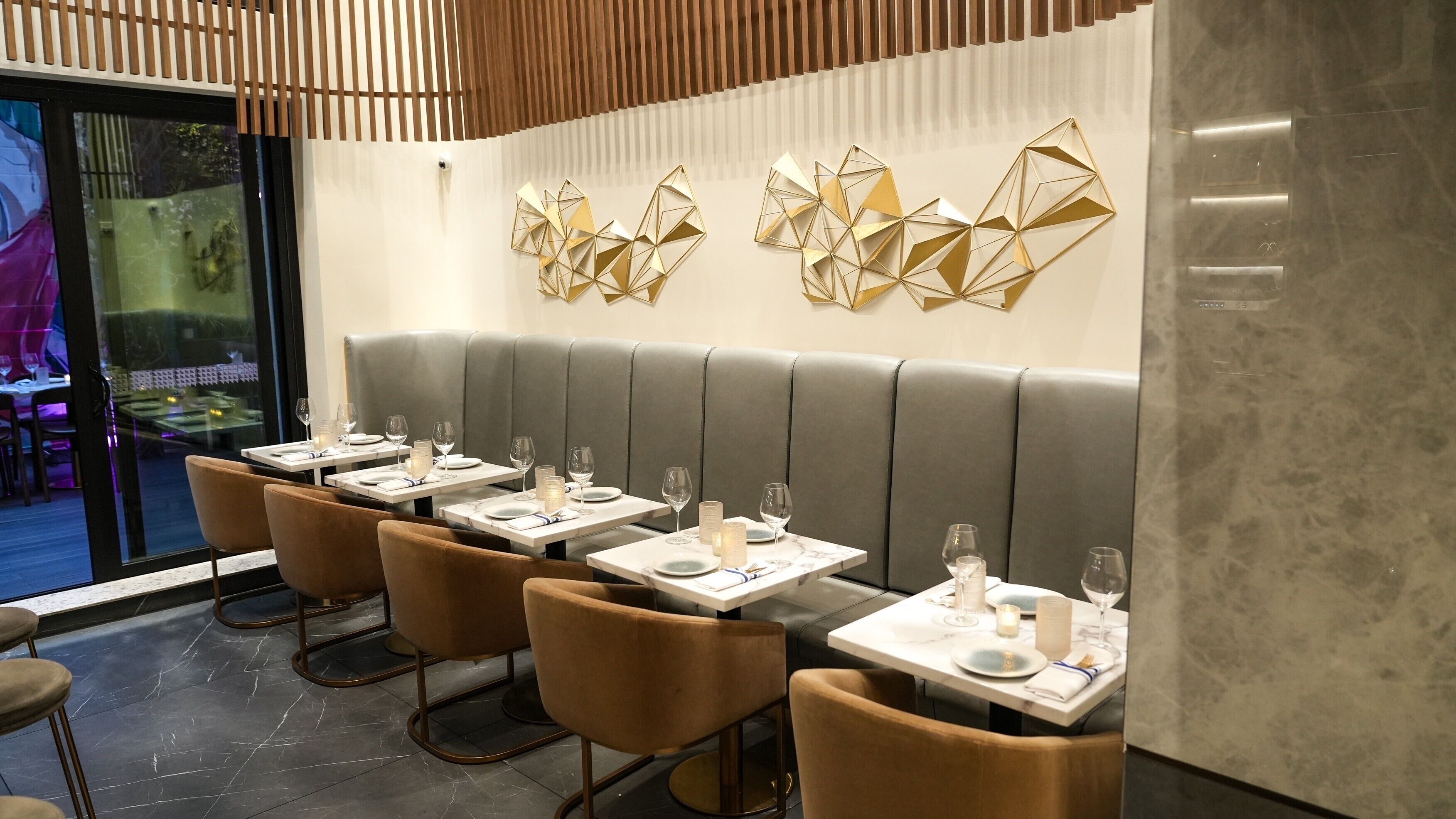 A restaurant interior with booth seating, marble-topped tables, and geometric wall art.