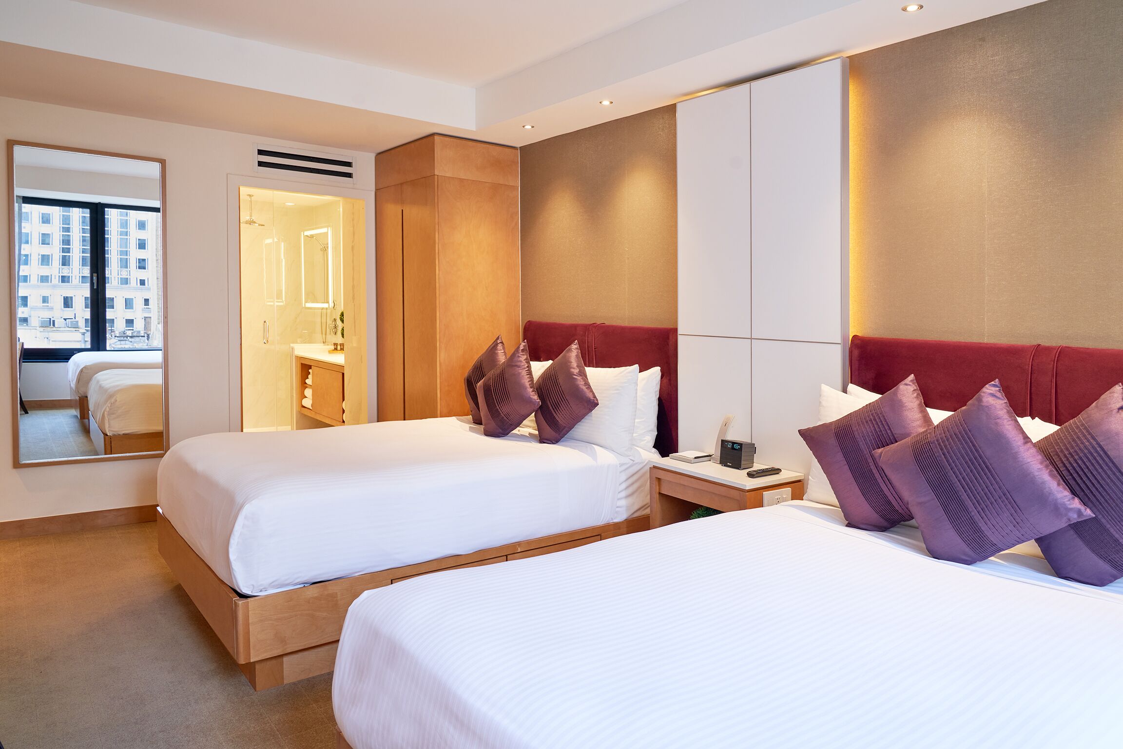 Habitación de hotel con dos camas, un espejo grande, tocador y vistas de la ciudad.