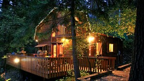 Una baita di legno con un patio, circondata da alberi e illuminata da luci decorative.