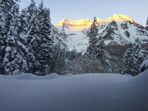 Escape to a serene winter wonderland surrounded by snow-covered mountains and dense evergreen trees.