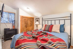 Cozy retreat with a neatly made bed, wooden wardrobe, and window with blinds.