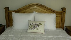 A bed with a wooden headboard, two white pillows, and a decorative pillow with a bird design.