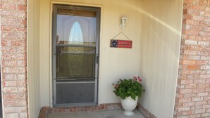 A front door with a screen door, a potted plant, and a sign that reads "AMERICA My home sweet home".