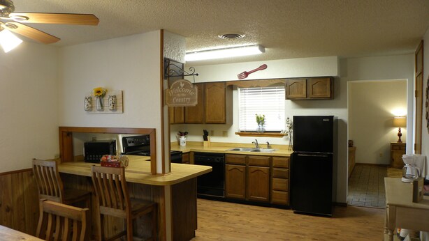 A compact kitchen with wooden cabinets, a black refrigerator, a microwave, and a dining area with a wooden table and chairs.