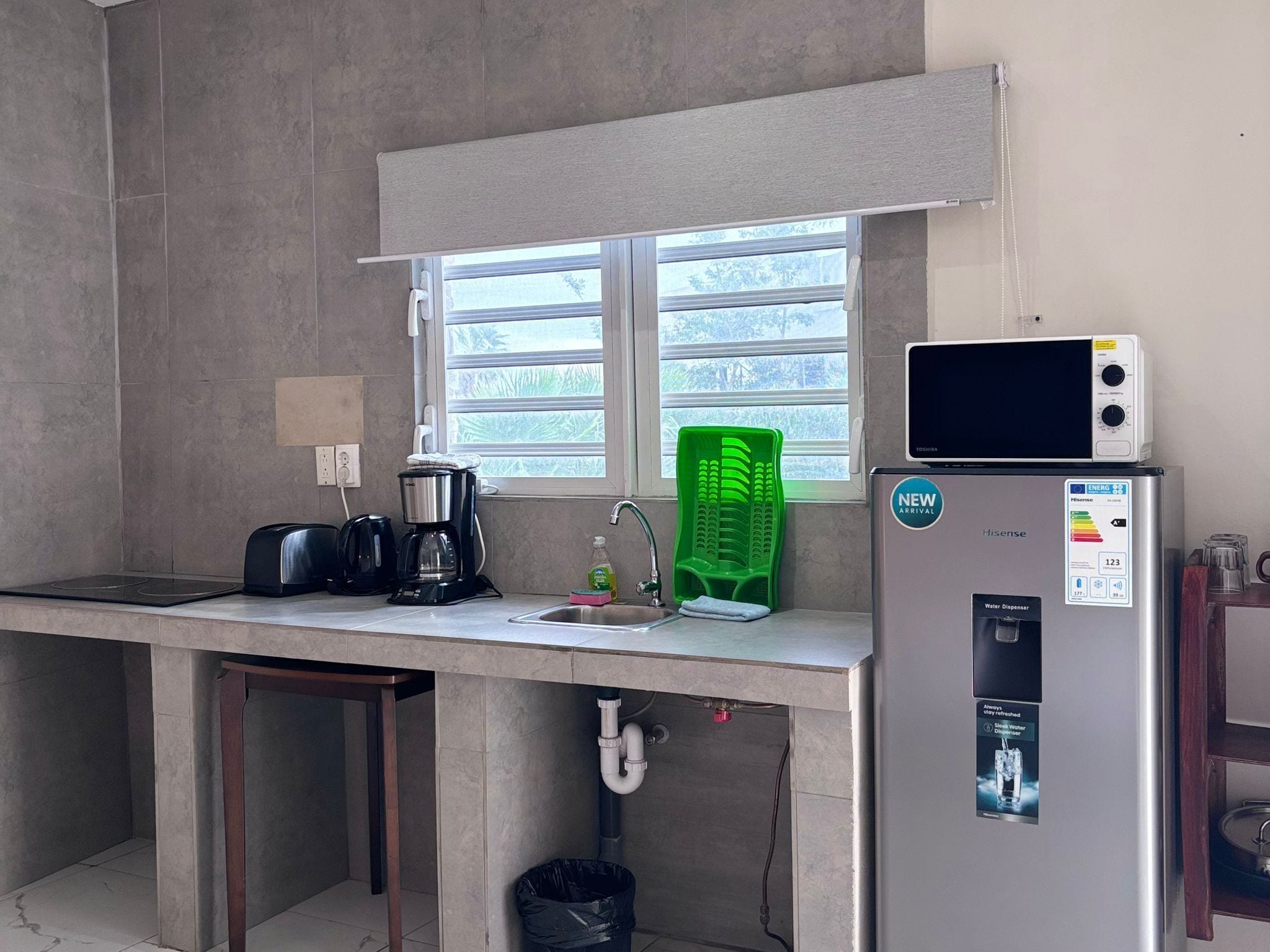 Eine kompakte Küche mit Spüle, Toaster, Kaffeemaschine, Mikrowelle und Wasserspender.