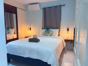 A hotel room with a bed, two bedside tables, an air conditioning unit, and a mirror. - Boca Simon Vacation Curacao (Willemstad)