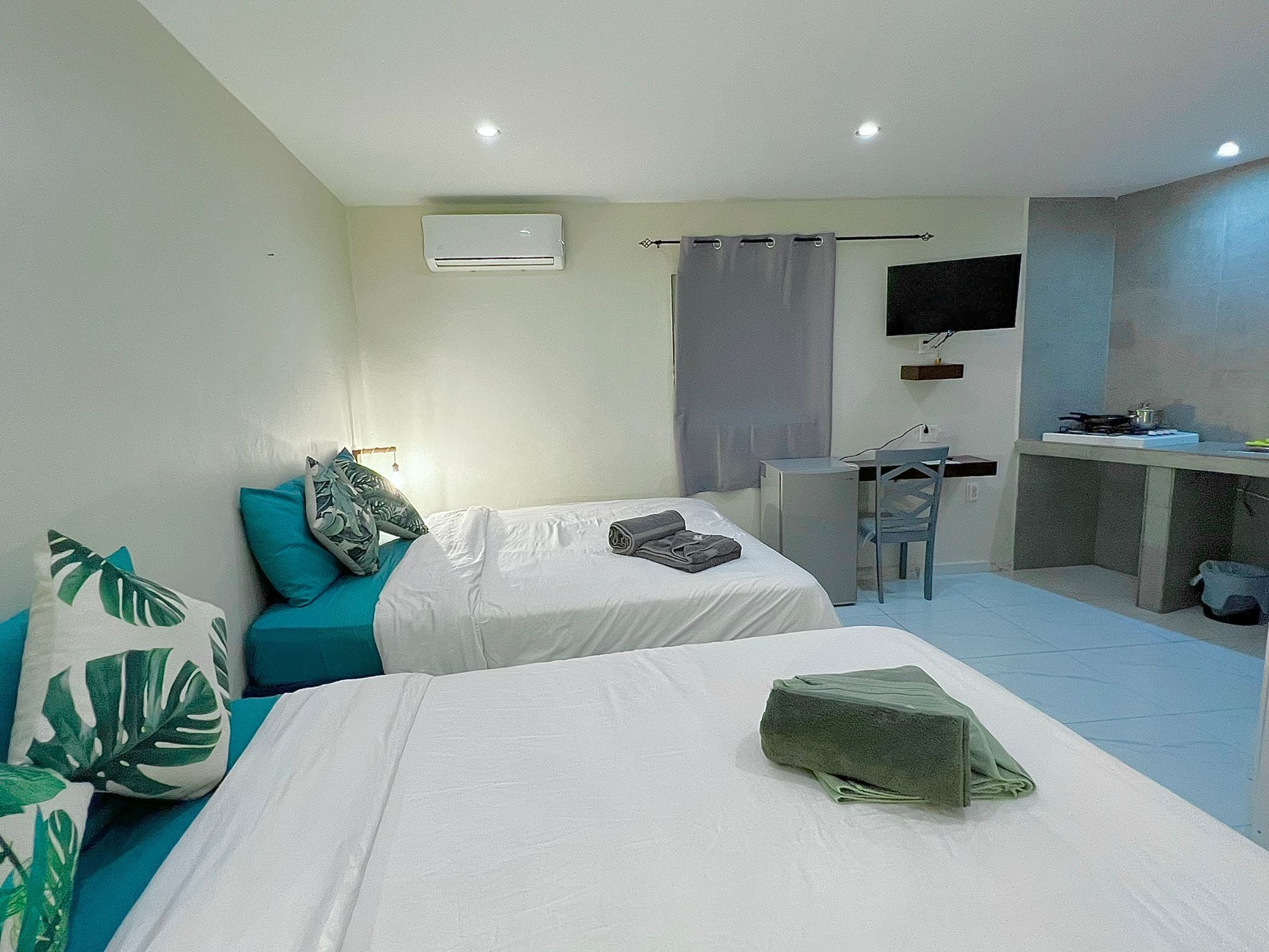 Une chambre d’hôtel avec deux lits, un bureau, une petite kitchenette et un téléviseur fixé au mur.