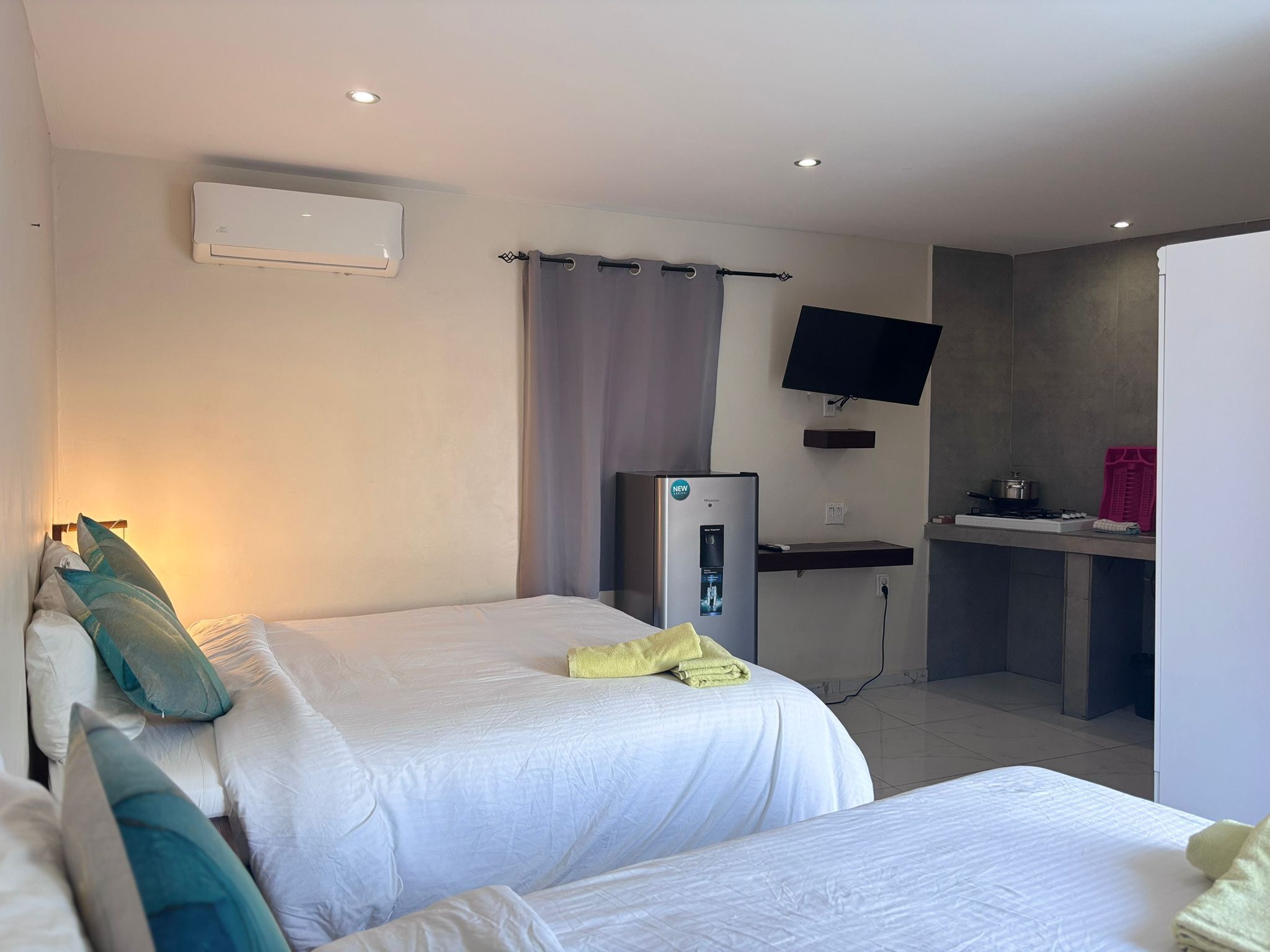 Une chambre d’hôtel avec deux lits, un téléviseur à écran plat fixé au mur, un réfrigérateur et un petit coin cuisine.