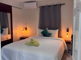 Una habitación de hotel con una cama, dos lámparas de noche, aire acondicionado y un espejo.