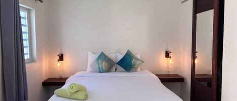 Habitación de hotel con cama, dos mesitas de noche, equipo de aire acondicionado, ventana con cortinas y puerta.