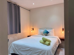 A hotel room with a bed, white bedding, two wall-mounted lamps, and a window with curtains. - Boca Simon Vacation Curacao (Willemstad)