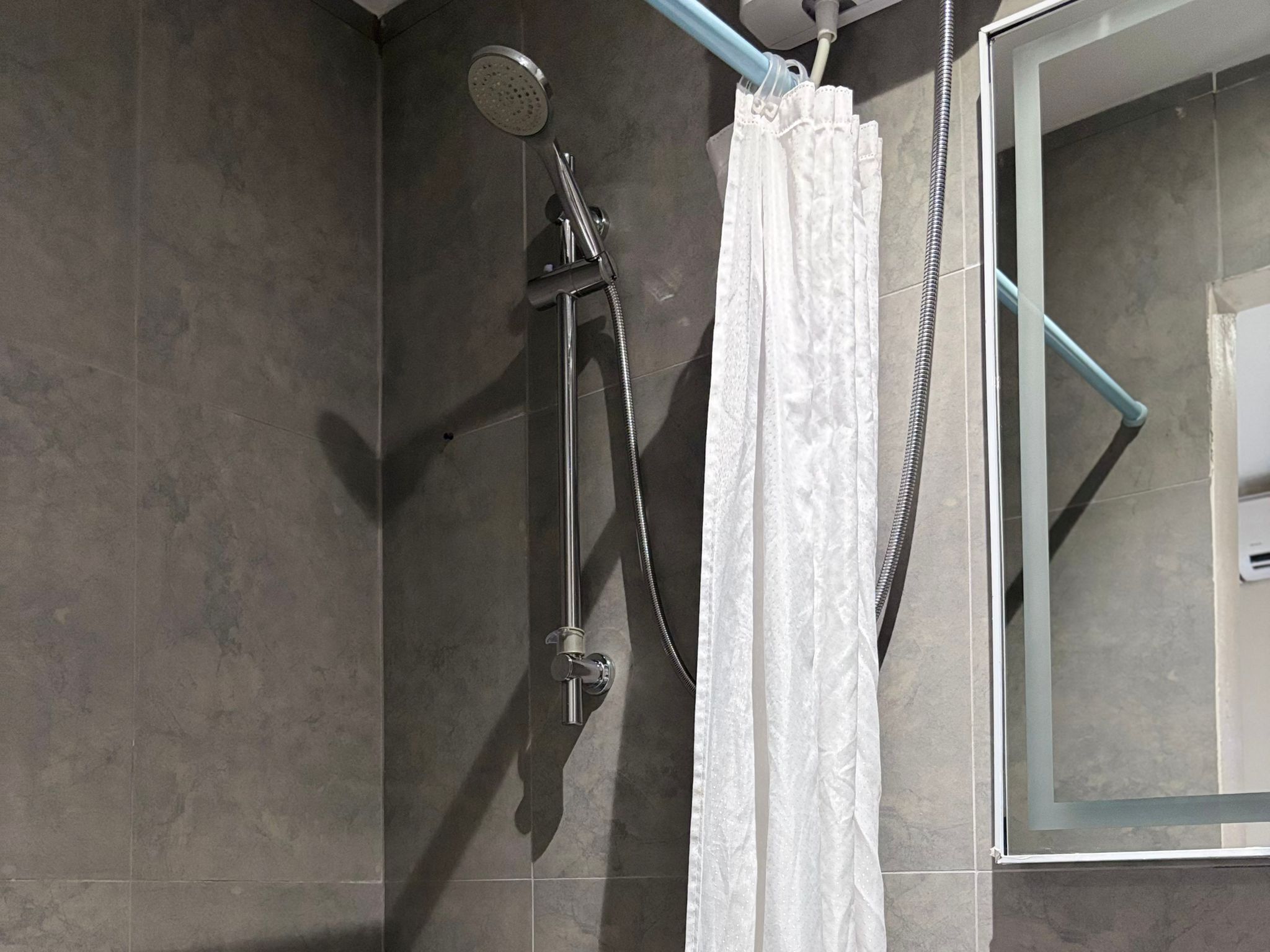 A shower with a handheld showerhead, a rain shower attachment, and a white shower curtain.