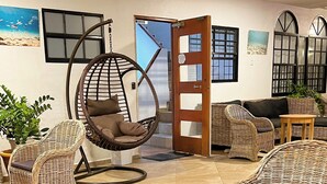 A room with wicker furniture, including chairs and a hanging chair, a wooden door, and a view of the outside. - Boca Simon Vacation Curacao (Willemstad)