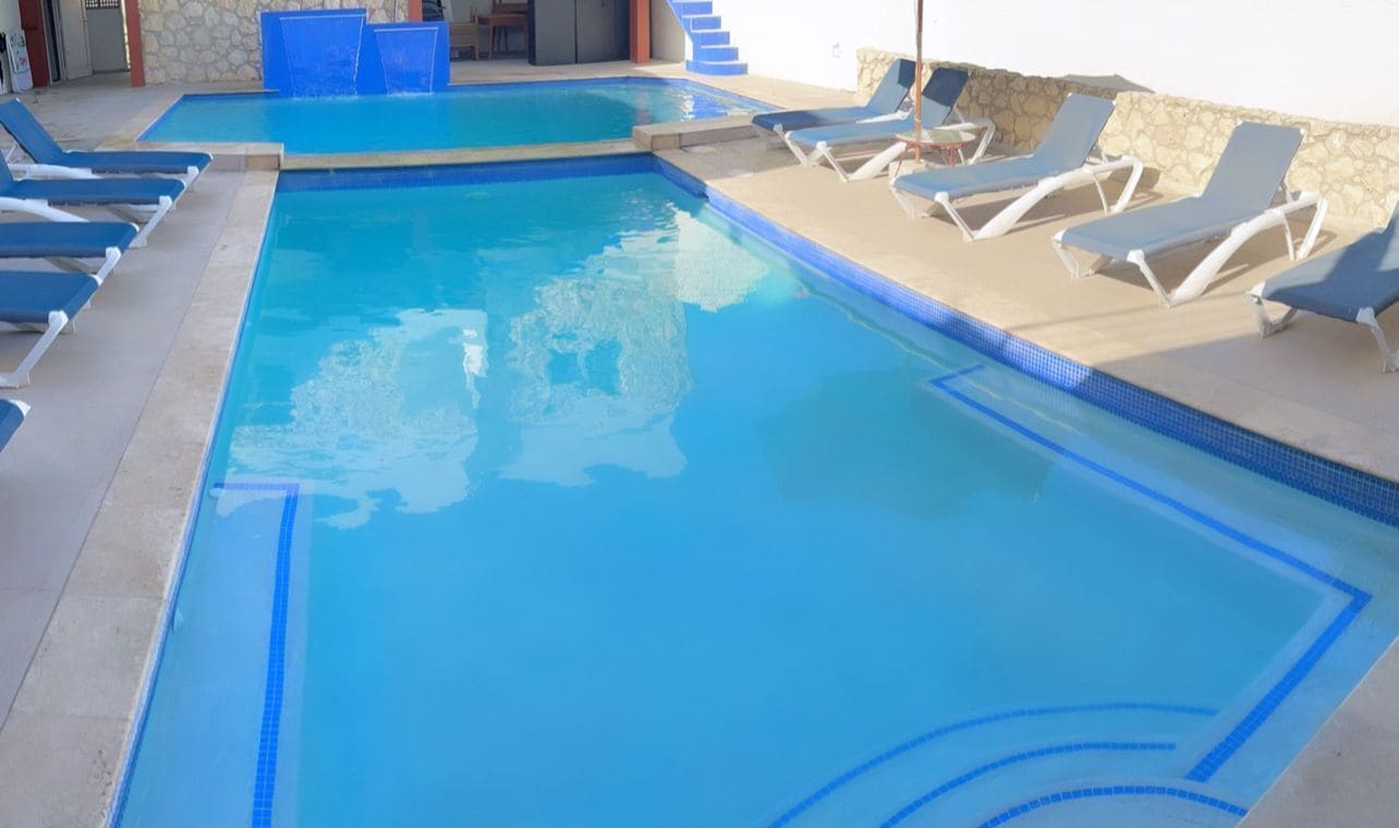 A swimming pool with blue tiles, lounge chairs, and a stone wall.