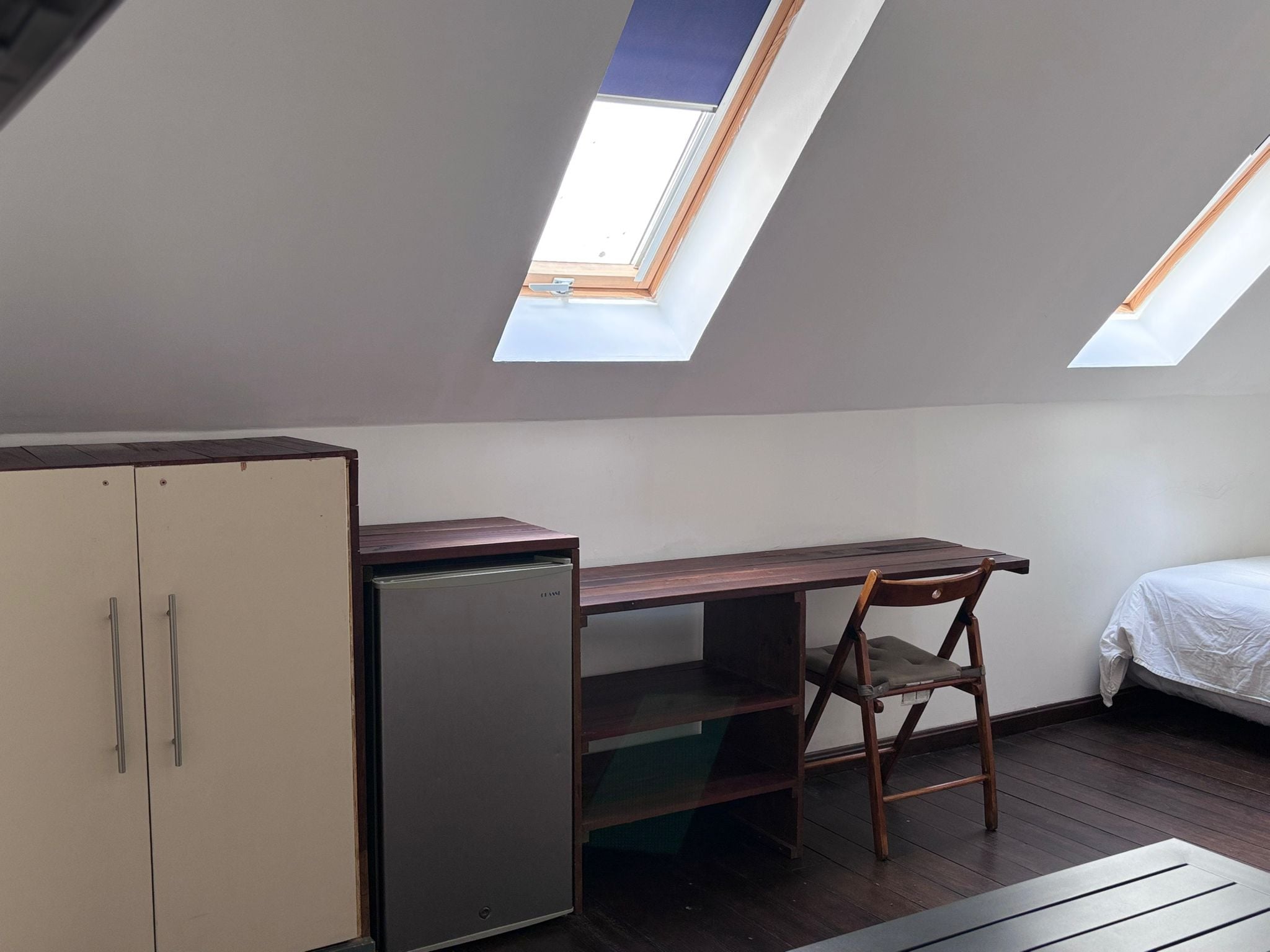 Una habitación pequeña y funcional con escritorio, silla, armario y dos tragaluces.