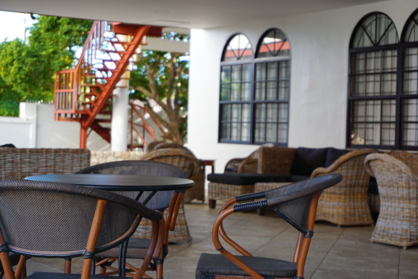 A covered outdoor seating area with wicker furniture and a staircase.