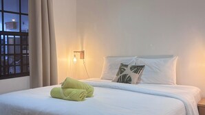 A neatly made bed with white linens and a green towel, a bedside lamp, and a window with a view of the outside. - Boca Simon Vacation Curacao (Willemstad)