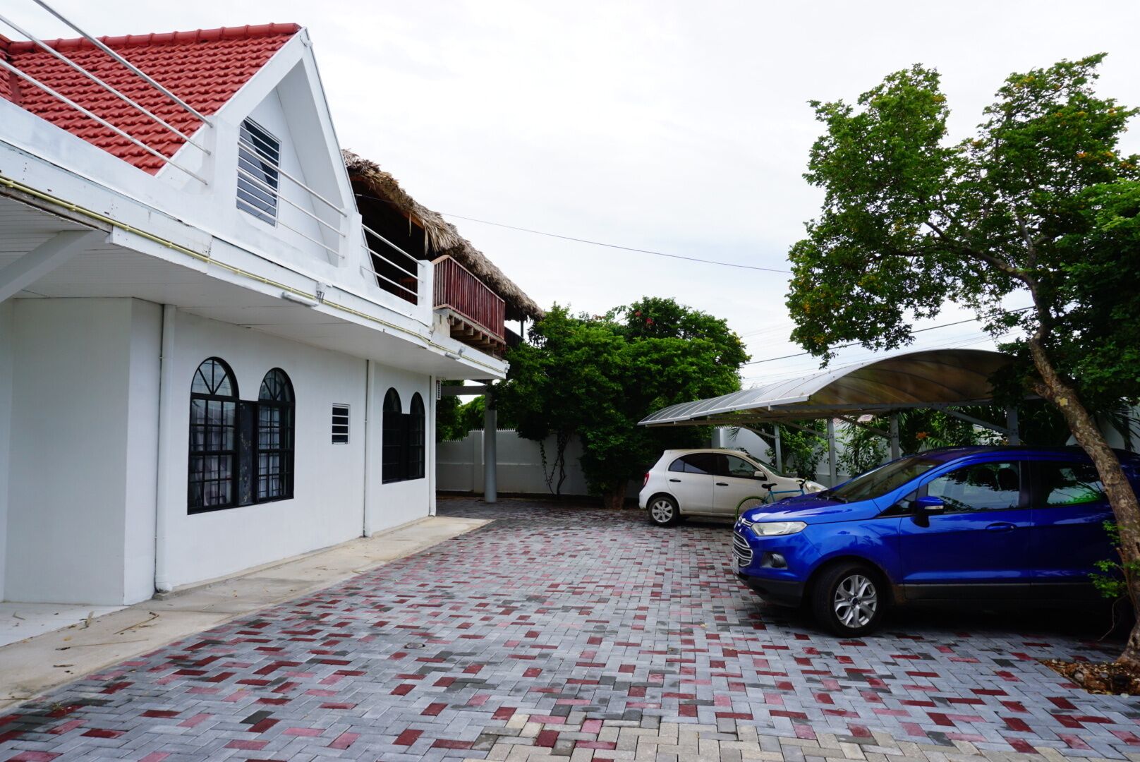 A white building with a red roof, a paved driveway, and two parked cars.