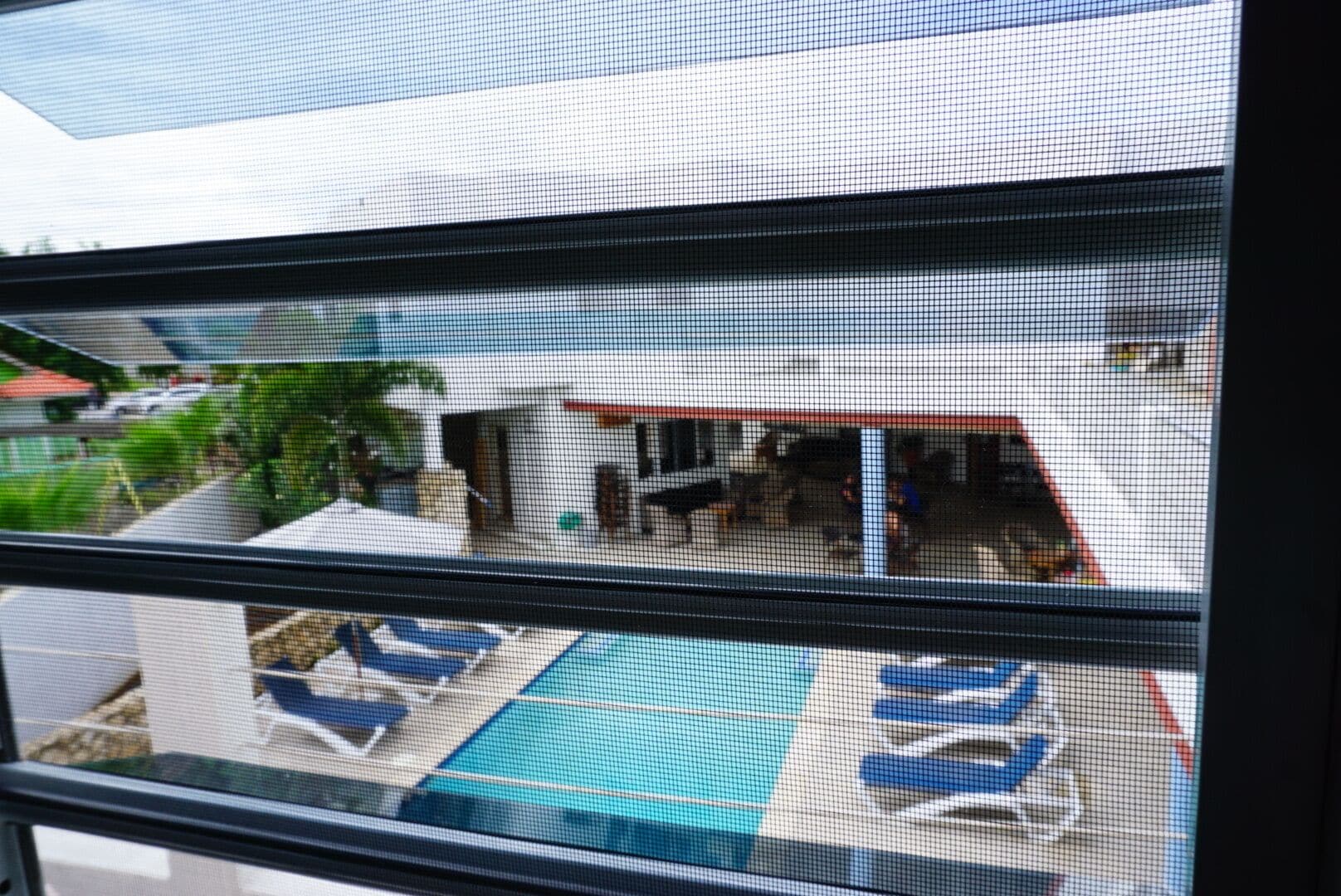 A view through a window with a pool area, including a lounge chair and a pool table.