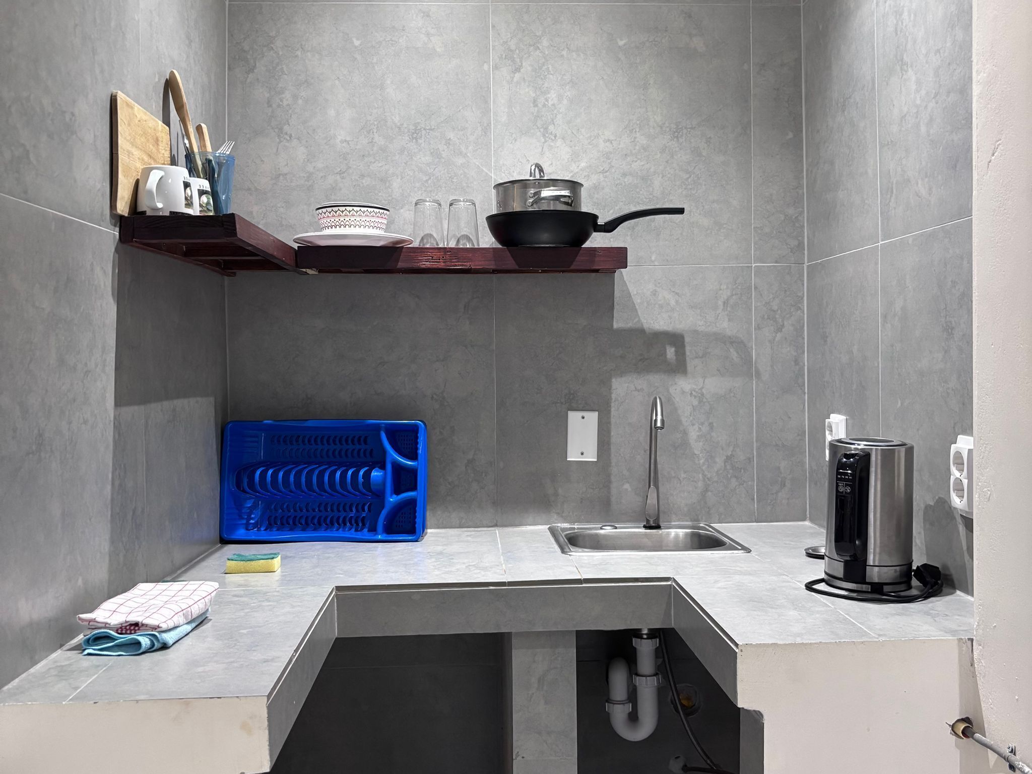 Una cucina compatta con lavello incassato, piano cottura e ripiano sopra il bancone con stoviglie.