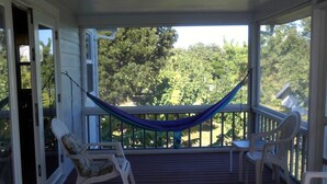 A covered porch with a hammock, two chairs, and a view of trees.