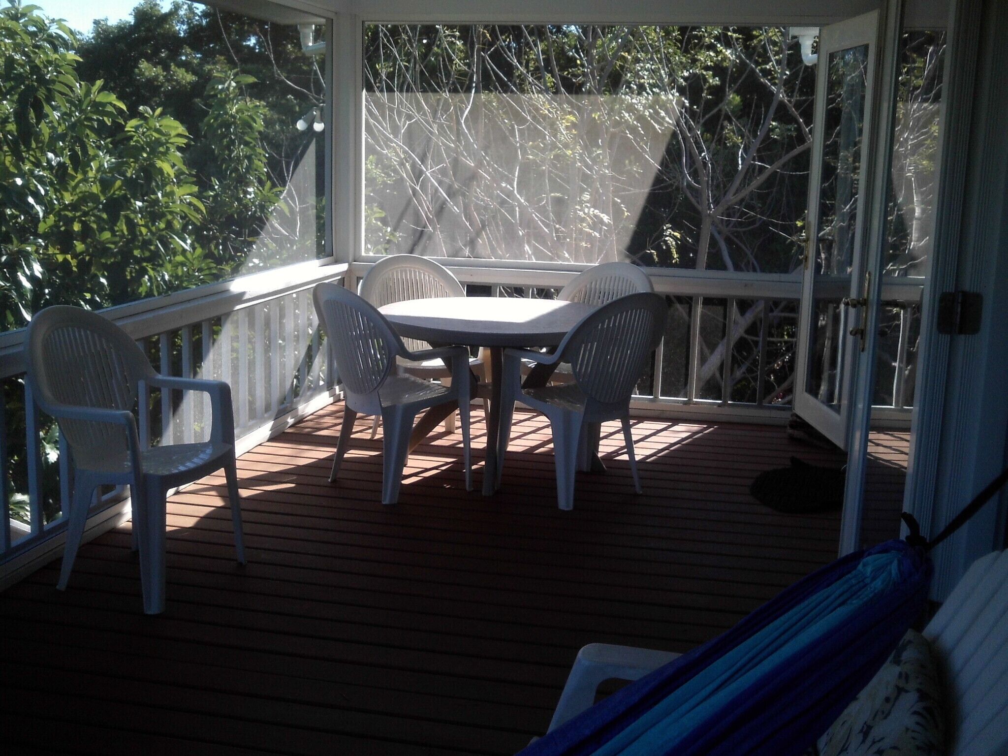 Eine überdachte Terrasse mit Tisch und vier Stühlen, umgeben von einer Holzterrasse und einem weißen Geländer.