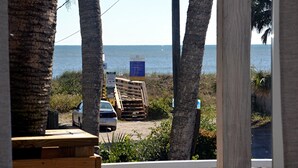 Vista de una playa con palmeras, un coche aparcado y una estructura de madera.