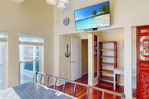 A spacious room with a large window, a wooden staircase, and a television displaying a beach scene.