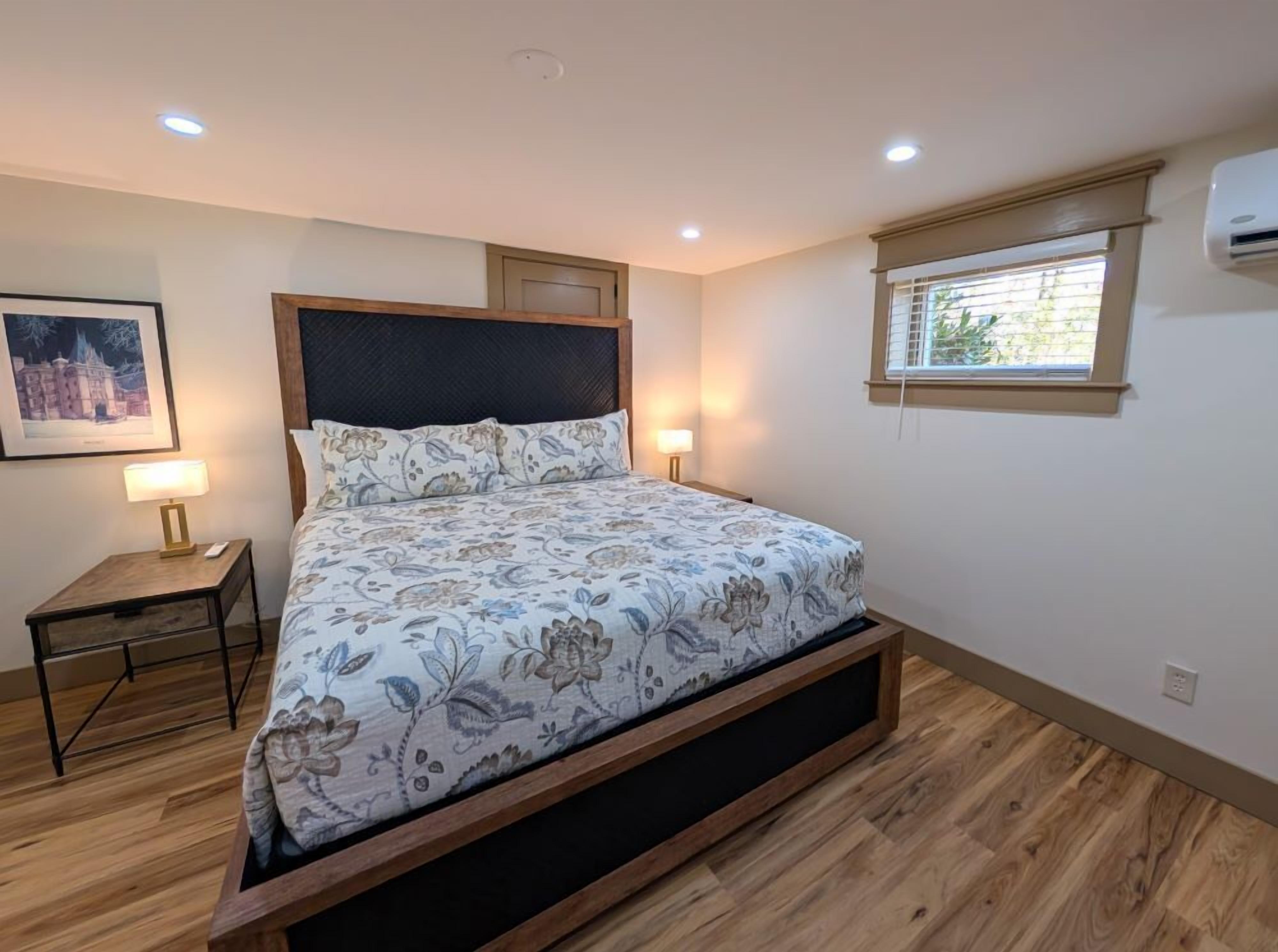 Un dormitorio con una cama, dos mesitas de noche con lámparas, una ventana con persianas y un aire acondicionado en la pared.