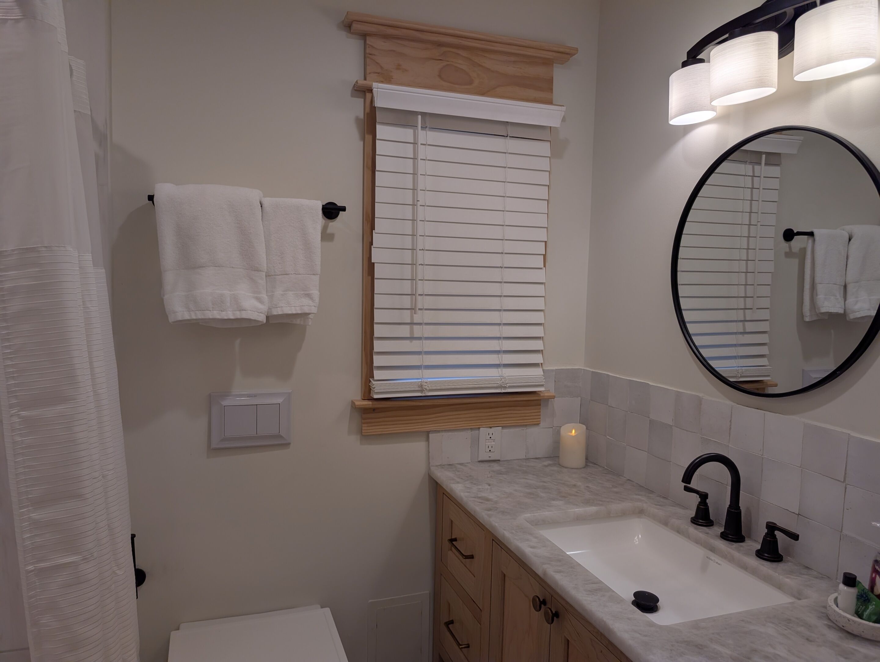Une salle de bain avec un lavabo, un miroir et une fenêtre équipée de stores.