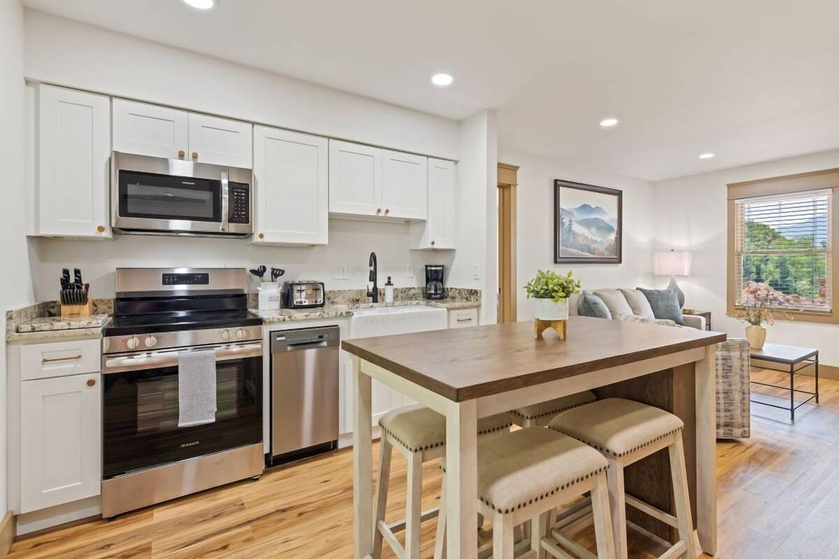 Una cocina moderna con armarios blancos, electrodomésticos de acero inoxidable y una mesa de comedor de madera con taburetes de bar.
