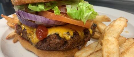 Ein Hamburger mit Salat, Tomate und Käse, dazu Pommes auf einem weißen Teller.