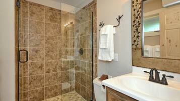 Une salle de bain avec une douche à parois de verre, un lavabo blanc et un meuble-lavabo en bois.