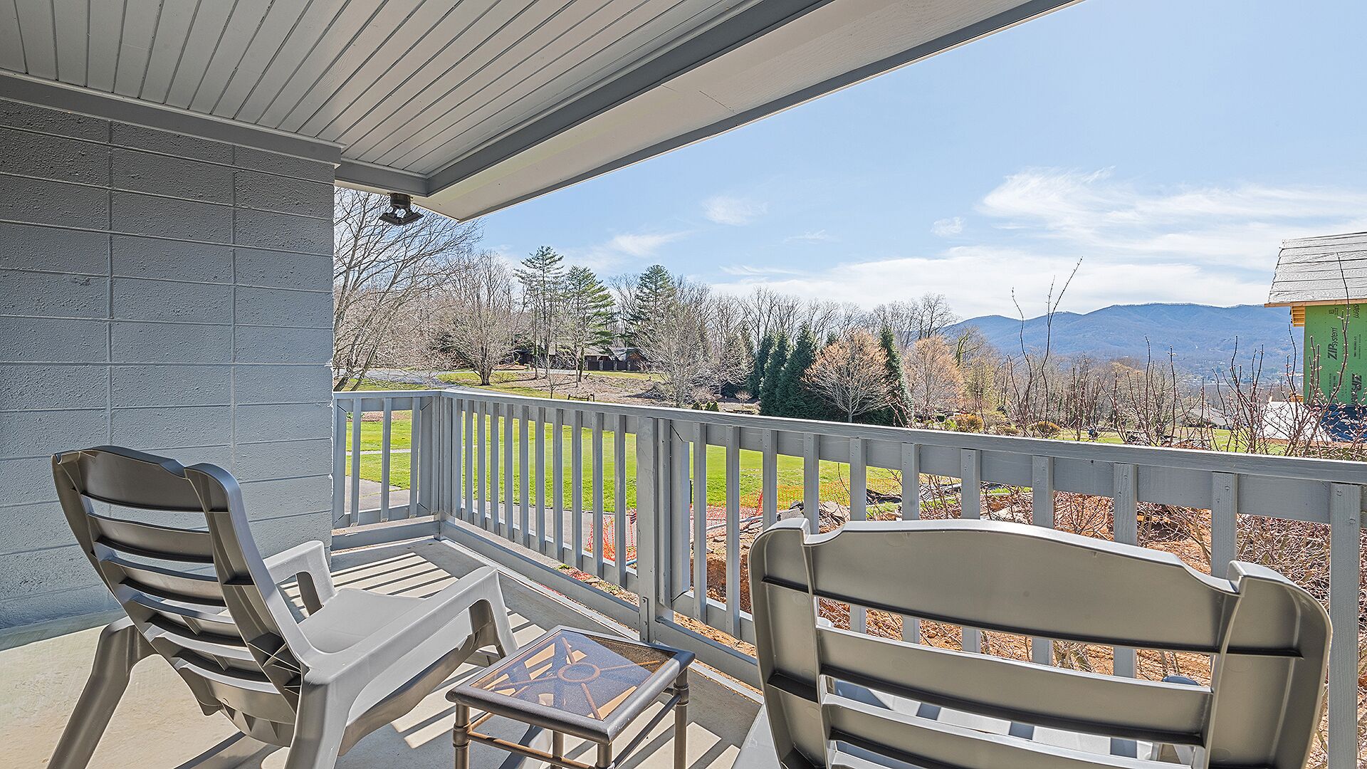 A covered outdoor area with two chairs and a small table, overlooking a landscaped yard and distant mountains.