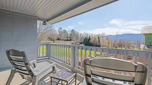 A covered outdoor area with two chairs and a small table, overlooking a landscaped yard and distant mountains.