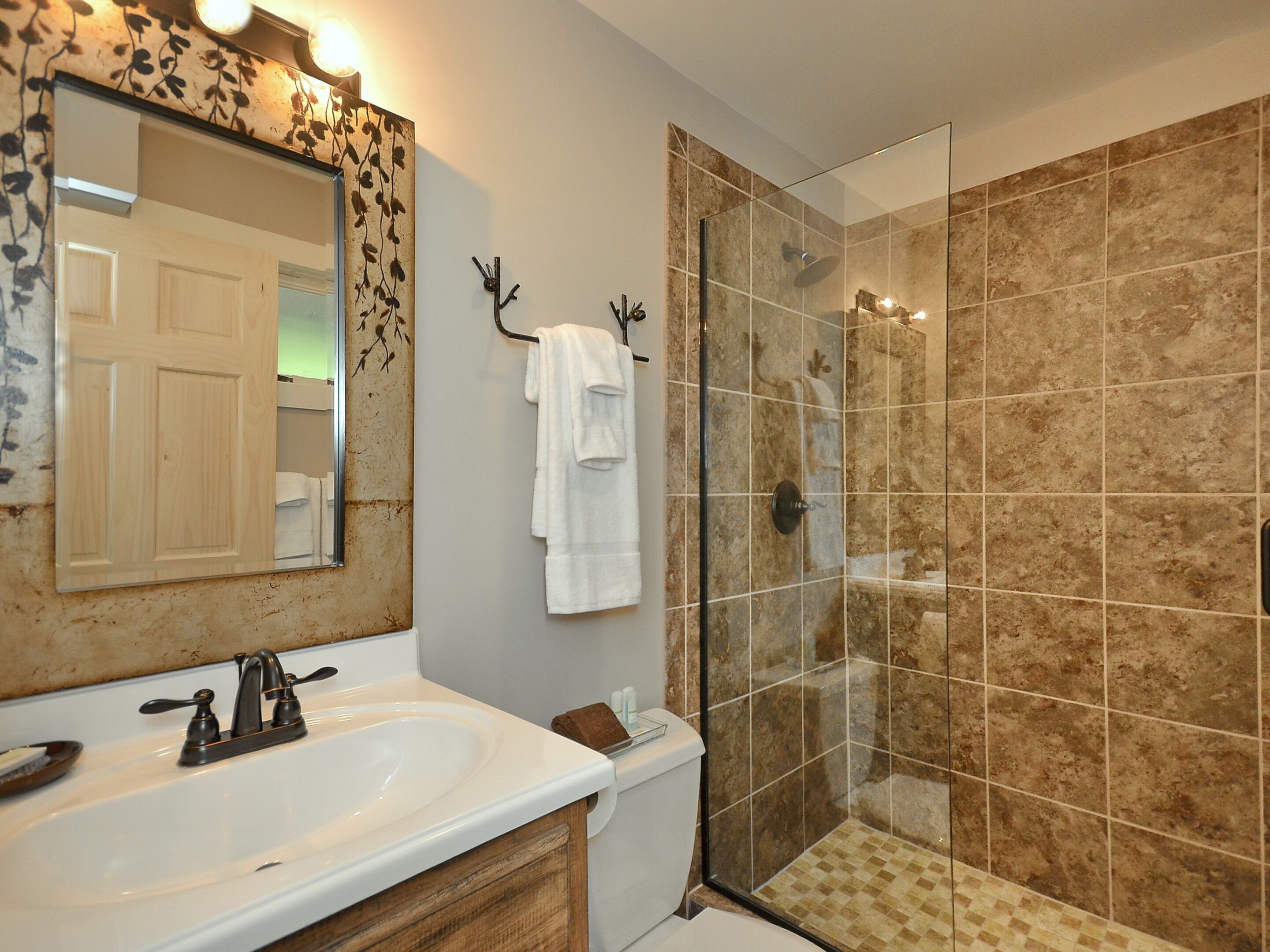 A bathroom with a white sink, a mirror with a decorative frame, a towel rack, and a glass-enclosed shower area.