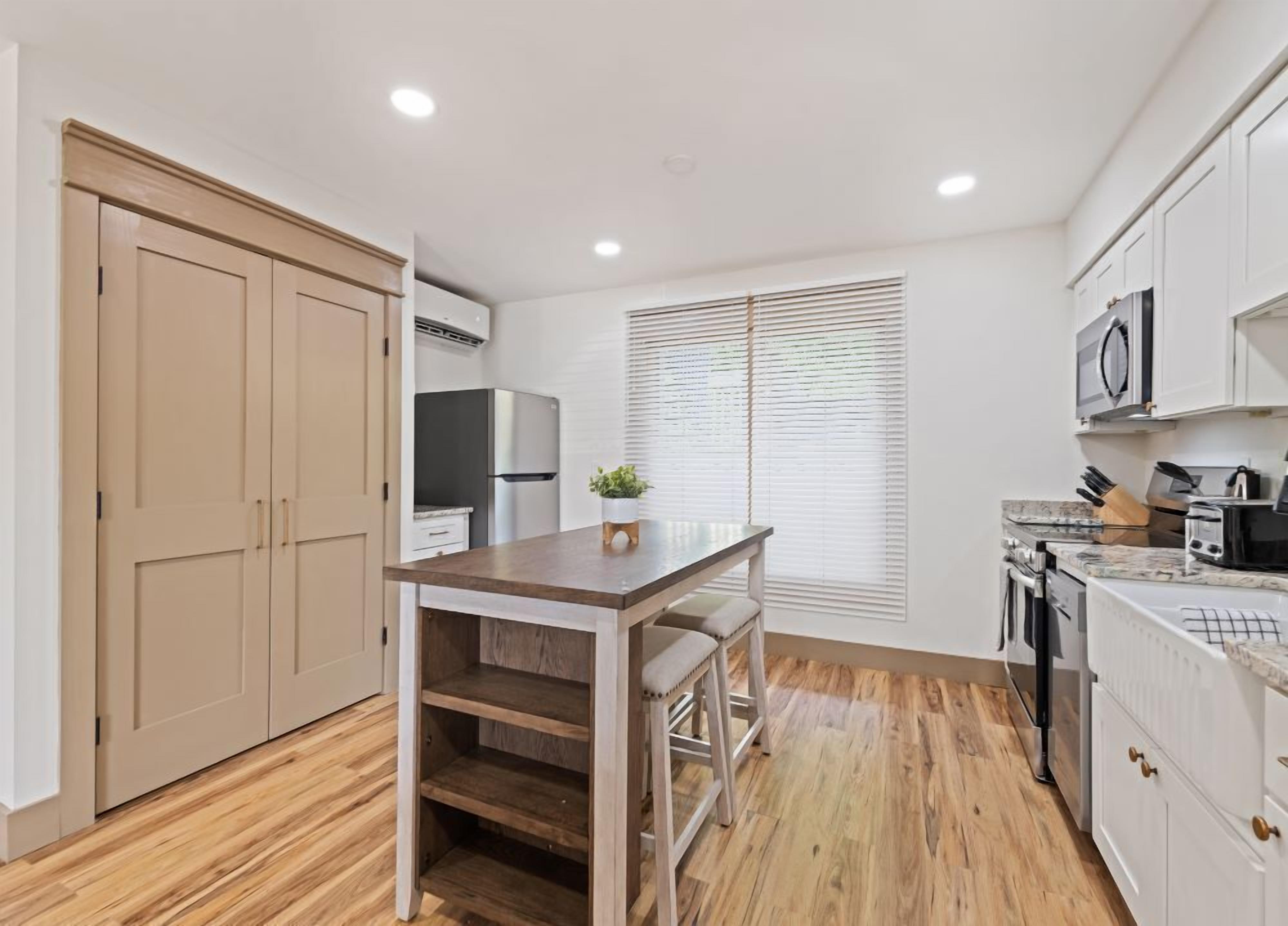 A compact kitchen with wooden flooring, white cabinets, a built-in oven, and a microwave.