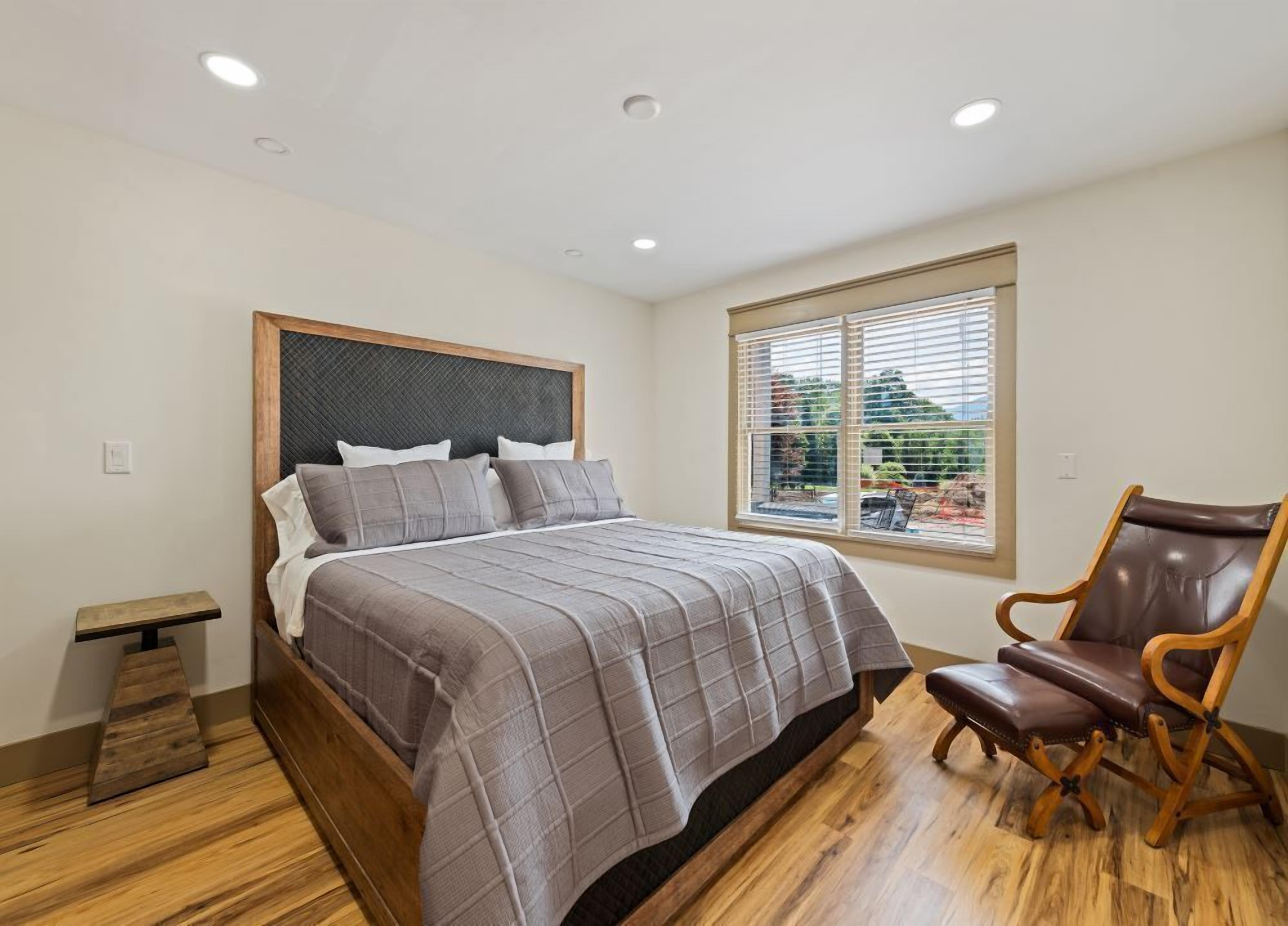 A bedroom with a bed, a wooden bench, a chair, and a window with blinds.