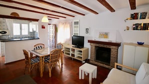 Una sala de estar con chimenea, televisor, una mesa de comedor con sillas y una estantería.