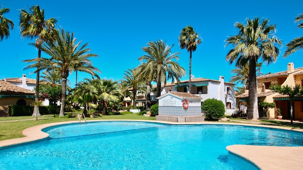 Una piscina rodeada de palmeras y edificios con tejados de cerámica.