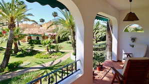 Un balcón con vistas a un jardín, una silla y una lámpara colgante.